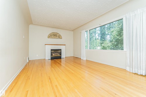 Hardwood flooring, fireplace with white mantel, and large picture window with extensive outdoor scenery - 8743 Strathearn Drive Nw, Edmonton, AB 