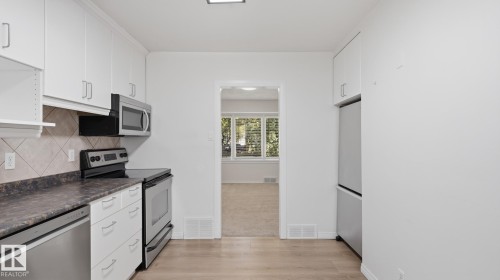 Kitchen featuring white cabinetry, stainless steel appliances, a tile backsplash, and wood-finish flooring - 11836 62 Street Nw, Edmonton, AB 