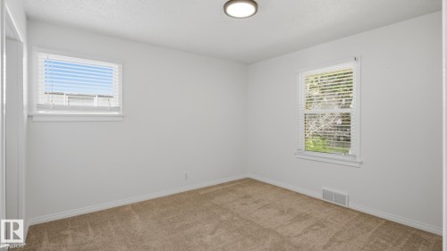 Bright room with two windows featuring horizontal blinds, neutral-toned carpet, and a flush-mount ceiling light fixture - 11836 62 Street Nw, Edmonton, AB 