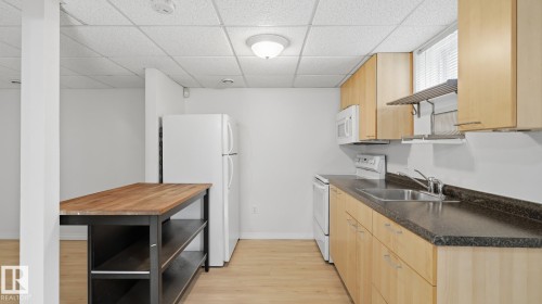 Kitchenette with light wood-finish cabinetry, dark countertops, and stainless steel sink - 11836 62 Street Nw, Edmonton, AB 