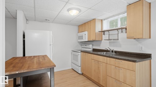 Kitchen featuring wood-finish cabinetry, white appliances, dark countertops, and wood-finish flooring - 11836 62 Street Nw, Edmonton, AB 