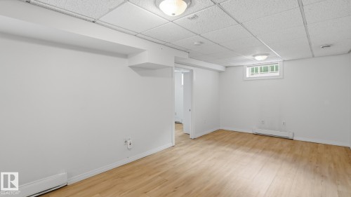 Spacious room featuring wood-finish flooring, white painted walls, and a dropped ceiling with integrated lighting - 11836 62 Street Nw, Edmonton, AB 