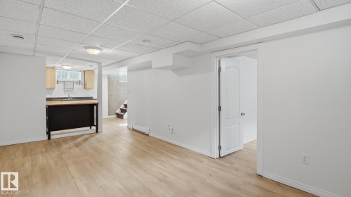 Wood-finish flooring, drop ceiling with recessed lighting, kitchen with wood cabinetry, and a white paneled interior door - 11836 62 Street Nw, Edmonton, AB 