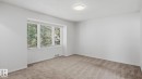 Neutral carpet flooring, white painted walls, large multi-pane window with blinds, and a flush-mount ceiling light fixture - 11836 62 Street Nw, Edmonton, AB 