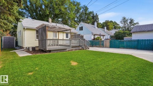 Expansive backyard featuring a manicured lawn, a large wood deck with a pergola, and a paved driveway - 11836 62 Street Nw, Edmonton, AB 