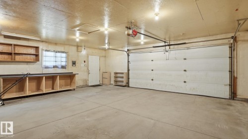 Spacious garage with concrete flooring, built-in shelving, an overhead door, and recessed lighting - 11836 62 Street Nw, Edmonton, AB 