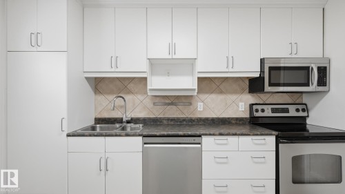 White cabinetry with stainless steel hardware, tile backsplash, and dark countertops - 11836 62 Street Nw, Edmonton, AB 