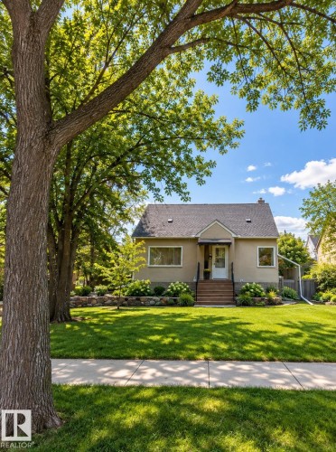 Stucco exterior with a peaked roofline, wood steps, and mature trees framing the property - 6542 112A Street Nw, Edmonton, AB 