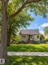 Stucco exterior with a peaked roofline, wood steps, and mature trees framing the property - 6542 112A Street Nw, Edmonton, AB 