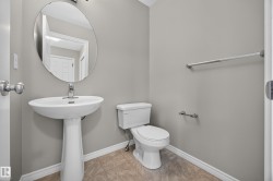 Pedestal sink with chrome faucet, oval wall mirror, toilet, and light gray wall paint - 
