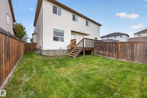 Rear exterior with light-colored siding, a wooden deck, and a wooden privacy fence enclosing a grassy yard - 483 Watt Boulevard Sw, Edmonton, AB 