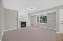 Recessed fireplace with tile surround and decorative mantel, large window with ample natural light, soft carpet flooring, and a built-in wall shelf - 483 Watt Boulevard Sw, Edmonton, AB 