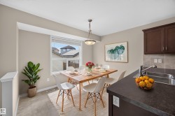 Recessed window with white blinds, wood-finish dining table, pendant light fixture, dark cabinetry, and a double basin stainless steel sink - 