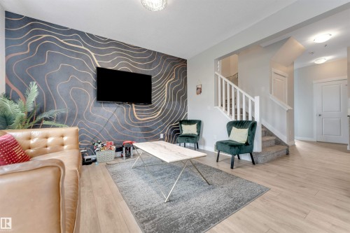 Accent wall with a modern abstract design, light wood-finish flooring, staircase with white risers and handrail, ceiling-mounted lighting fixtures, and solid panel interior doors - 2004 15 Avenue Nw, Edmonton, AB 