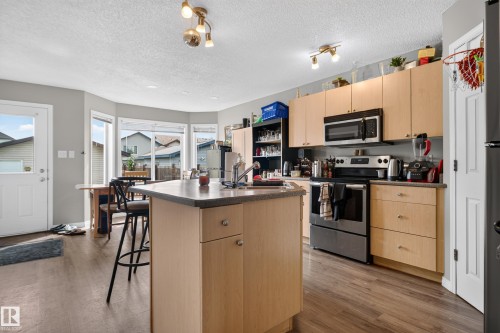 Kitchen featuring wood-finish flooring, stainless steel appliances, light-toned cabinetry, and a center island with a sink - 7817 Schmid Place Nw, Edmonton, AB 