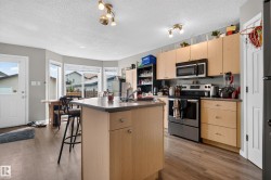 Kitchen featuring wood-finish flooring, stainless steel appliances, light-toned cabinetry, and a center island with a sink - 