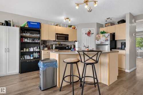 Kitchen featuring an island with counter seating, wood-finish flooring, light wood-finish cabinetry, and stainless steel appliances - 7817 Schmid Place Nw, Edmonton, AB 