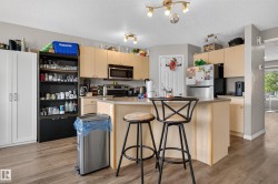 Kitchen featuring an island with counter seating, wood-finish flooring, light wood-finish cabinetry, and stainless steel appliances - 
