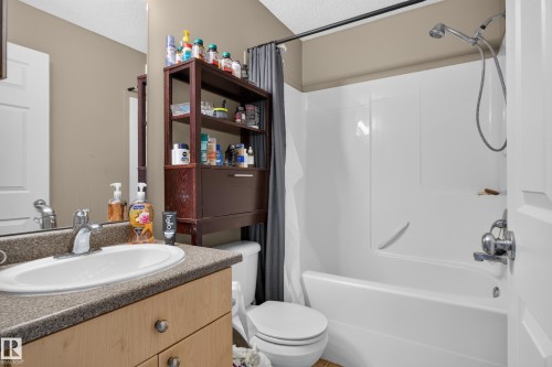 Spa-inspired bathroom featuring a wood-finish vanity with gray stone countertop, white porcelain sink, and polished chrome faucet - 7817 Schmid Place Nw, Edmonton, AB 