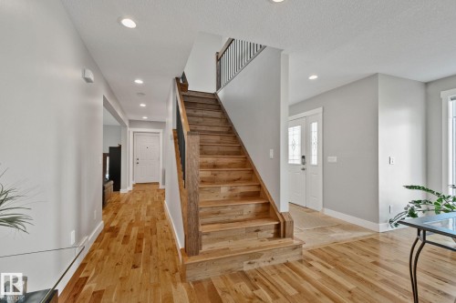 Hardwood flooring, recessed ceiling lighting, a wood staircase with black iron balusters, and a double-door entry with decorative glass inserts - 12403 29A Avenue Nw, Edmonton, AB 