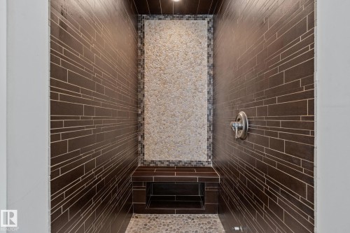 Walk-in shower with stone tile accent wall, built-in bench, recessed shelf, and pebble flooring - 12403 29A Avenue Nw, Edmonton, AB 
