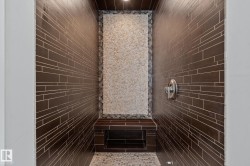 Walk-in shower with stone tile accent wall, built-in bench, recessed shelf, and pebble flooring - 