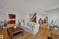 Hardwood flooring, recessed lighting, a built-in wet bar with wood cabinetry, and a wood staircase with dark railing - 