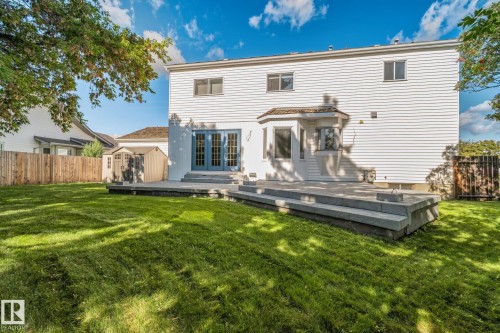 Expansive rear yard featuring a manicured lawn, multi-level stone patio, and white siding exterior with a bay window - 12403 29A Avenue Nw, Edmonton, AB 