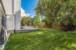 Spacious lawn area with mature trees, a multi-level concrete patio, and a wood privacy fence - 