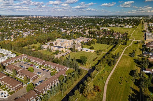 Expansive aerial perspective showcasing a residential development with multiple units, a large institutional building, abundant green spaces, and an extensive network of paved pathways - 12403 29A Avenue Nw, Edmonton, AB 