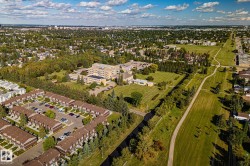 Expansive aerial perspective showcasing a residential development with multiple units, a large institutional building, abundant green spaces, and an extensive network of paved pathways - 