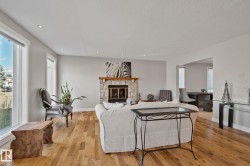 Spacious living area featuring wood-finish flooring, a stone fireplace with a wood mantle, and recessed lighting - 