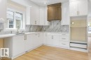 Contemporary kitchen featuring white cabinetry with brushed gold hardware, marble-look tile backsplash, and stainless steel built-in appliances including a dishwasher - 10323 79 Street Nw, Edmonton, AB 