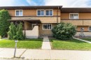 Two-story townhome with stucco and horizontal siding exterior, covered entry porch, white frame windows, and a concrete walkway - 155 Woodborough Way Nw, Edmonton, AB 