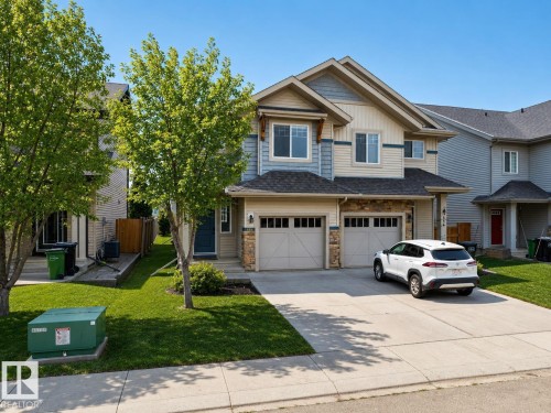 Two-story exterior with stone accents, dual garage doors, a concrete driveway, and mature landscaping - 1668 Chapman Way Sw, Edmonton, AB 