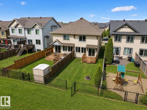 Expansive fenced backyard featuring a manicured lawn, a built-in fire pit, and a wooden deck structure - 1668 Chapman Way Sw, Edmonton, AB 