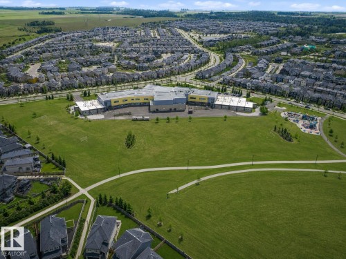 Expansive community green space with paved walking paths, a dedicated sports field, and a playground area, surrounded by residential properties and a central community building - 1668 Chapman Way Sw, Edmonton, AB 