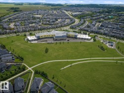 Expansive community green space with paved walking paths, a dedicated sports field, and a playground area, surrounded by residential properties and a central community building - 
