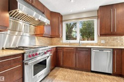 Gourmet kitchen featuring a stainless steel range and hood, wood cabinetry, stone countertops, and tile flooring - 