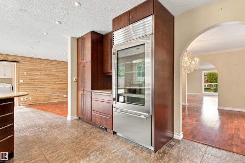 Integrated stainless steel refrigerator, custom wood cabinetry, tiled flooring, wood-finish flooring, and arched doorway - 14103 60 Avenue Nw, Edmonton, AB 