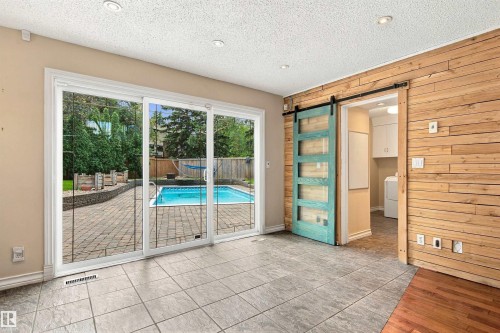 Expansive sliding glass doors, paver patio, in-ground swimming pool, wood-paneled accent wall, and a turquoise barn door - 14103 60 Avenue Nw, Edmonton, AB 