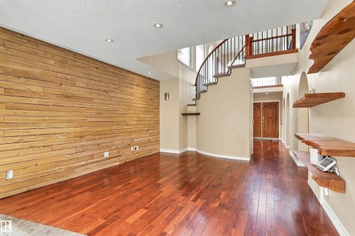 Wood-finish flooring throughout, featuring a wood-paneled accent wall, recessed lighting, and a curved staircase with wrought iron balusters - 14103 60 Avenue Nw, Edmonton, AB 
