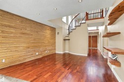 Wood-finish flooring throughout, featuring a wood-paneled accent wall, recessed lighting, and a curved staircase with wrought iron balusters - 