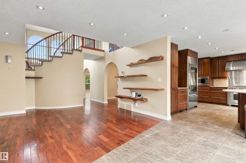 Open-concept interior featuring wood-finish flooring, a curved staircase with wrought iron railing, arched doorways, a kitchen with stainless steel appliances, and built-in wood shelving - 14103 60 Avenue Nw, Edmonton, AB 