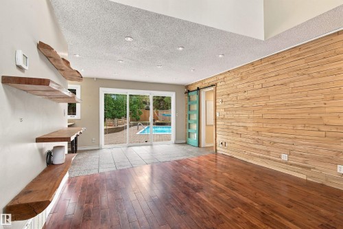 Hardwood flooring, wood accent wall, built-in wooden shelving, recessed lighting, and sliding glass doors to outdoor pool - 14103 60 Avenue Nw, Edmonton, AB 