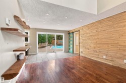 Hardwood flooring, wood accent wall, built-in wooden shelving, recessed lighting, and sliding glass doors to outdoor pool - 