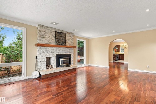 Wood-finish flooring, stone-clad fireplace with wood mantle, recessed lighting, and arched doorway - 14103 60 Avenue Nw, Edmonton, AB 