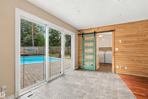 Sliding glass door to backyard with swimming pool and paver patio, wood panel accent wall, and a barn door entry - 14103 60 Avenue Nw, Edmonton, AB 