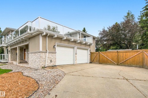 Stucco exterior with stacked stone accents, glass panel railings, two-car garage, and a wood privacy fence - 14103 60 Avenue Nw, Edmonton, AB 