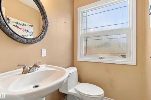 Pedestal sink with brushed nickel faucet, dual-pane window with privacy glass, decorative window grilles, and a round ornamental mirror - 14103 60 Avenue Nw, Edmonton, AB 